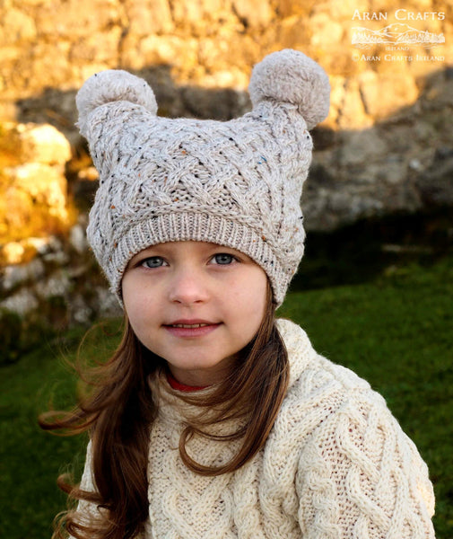 Children's Pom Pom Hat in Oatmeal - 100% Merino Wool knitted hat with two pom poms for child, on model