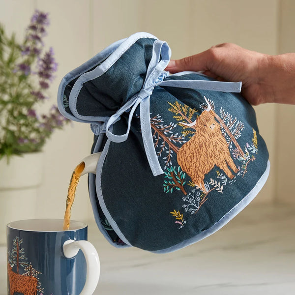 Connie the Cow Tea Cosy shown in use with a tilted teapot pouring tea into a Connie the Cow mug.