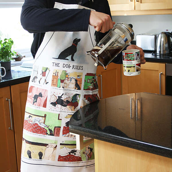 Person pouring coffee from a French press into a mug, wearing an apron with a dog-themed design.