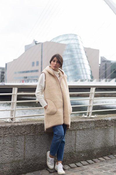 Model wearing the beige Barbara Vest on a bridge next to a river.