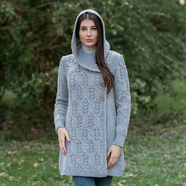 Woman wearing a gray knitted coat with a hood outdoors.