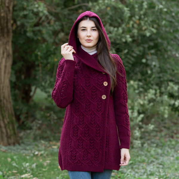 Woman wearing a wine coloured knitted coat with a hood in a forest setting
