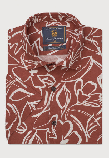 Up close view of the folded rust coloured floral cotton linen short sleeved shirt.
